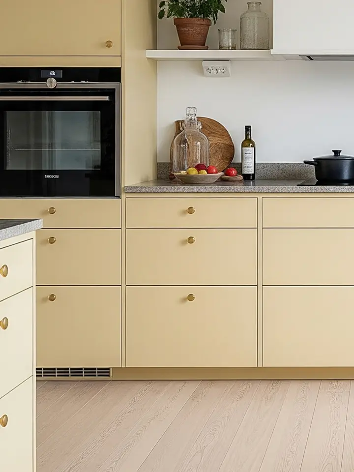 Mjukt gult kök med ramluckor, ljusa trägolv och bänkskiva i sten