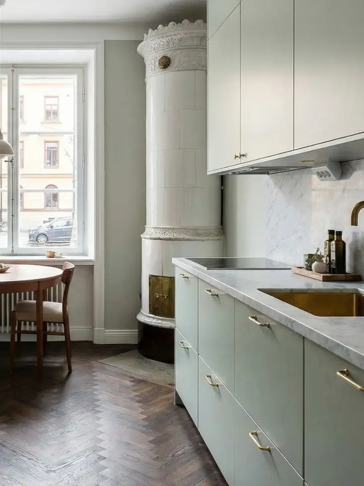 Ljusgrönt kök med ramluckor, marmorbänkskiva och klassisk kakelugn